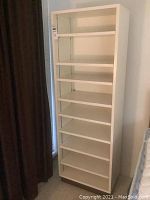 Front view of the tall white shelving unit against a wall with a curtain beside it.