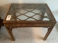 Front view of rattan side table showing woven detailing and glass top with lattice pattern beneath.