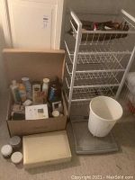 Photo showing white metal storage rack with wire baskets, Salter weighing scale with a white plastic bin on top, and a box containing assorted bath accessories and beauty products.