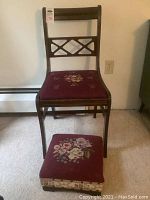 Full view of vintage wooden chair with burgundy needlepoint seat and matching footstool with floral needlepoint top.