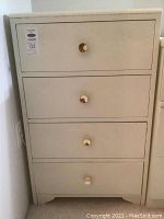 Front view of the cream/white painted dresser showing four drawers each with a single round gold knob.