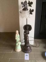 Full view of the vintage metal lamp and ceramic lady statuette side by side on tiled floor.