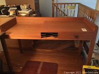 Wood writing desk with a single drawer and open mail slot, medium brown finish, set on hardwood floor near banister.