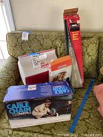 Photo showing Shur Grip cable chains box in front with a woman installing chains illustration, Igloo Playmate cooler, auto sun fans box, and plastic floor lamp tall box all on a green patterned sofa.