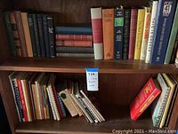 Shelf with a mix of vintage hardback books including cookbooks, classic literature and reference books.