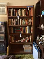 Front view of the wooden bookshelf filled with books for scale only. Shows five shelves in medium brown wood finish. Dimensions 36x12x72 as per seller.