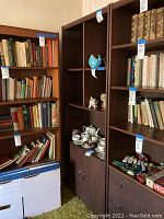Photo showing bookshelf and neighboring shelves filled with books, small decorative items, and china tea set. Focus on bookshelf's size, shelving layout, and lower cabinet.