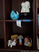 Shelf with six decorative and collectible items including ceramic bust, blue vase, pig figurine, Buddha figurine, Santa figurine, and tin box