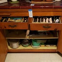 Kitchen drawers with silverware, barware, linens, and cookware visible with cabinet doors open