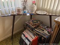 Photo of wooden corner table with decorative ceramic pots, glass vase, silver plate on top and vinyl records underneath