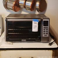 Frontal view of stainless steel DeLonghi convection oven showing door, control panel, and racks inside.