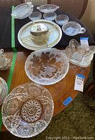 Wide view of assortment of glass serving bowls, platters, hors d'oeuvre tray, and covered dish on wooden surface