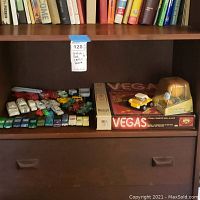 Shelf showing multiple diecast toy cars arranged in rows including fire trucks, ambulances, and various sedans alongside a boxed game and McDonald's toy.