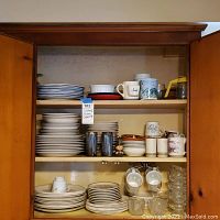 Full view of kitchen cupboard shelves showing stacked plates, mugs, bowls, and glasses.