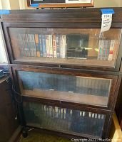 Front view of the lawyer bookcase showing three glass-front compartments filled with VHS tapes.
