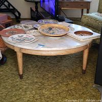 Full view of the round wood coffee table with white marble top and various decorative plates on top.