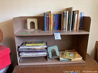 Metal bookshelf with books arranged on top shelf and magazines with bookends on bottom shelf