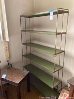 Front view of metal bookshelf with six green shelves and bronze/gold metal frame.