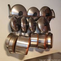 Photo showing hanging Revere Ware pots and pans with lids on wall rack, copper-clad bottoms visible, various sizes