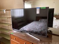 Front view of Samsung TV with stand showing reflective screen and part of room reflected on screen.