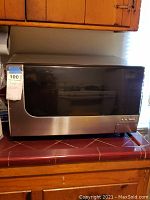 Front view of the Sharp microwave showing the stainless steel and black door with control buttons and digital display.