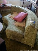 Side view of vintage green curved sofa with two beige throw pillows with fringe and one pink throw pillow on it.