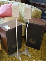 Two vintage wood speakers with black grills sitting on the floor behind two silver metal stands with small, textured silver Sony speakers mounted on top.