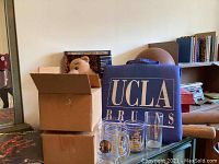 Wide view showing cardboard boxes, plush bear, UCLA chair, glass mugs, and wooden bats