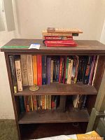 Full view of wood bookshelf filled with books on the two shelves and stacked on top.