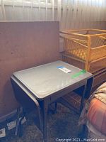 Gray vintage card table with metal legs folded, showing wear and placed on floor