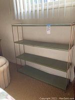 Front view of the vintage metal bookshelf showing four green flat shelves and gold-tone tubular metal frame.