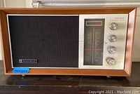 Front view showing wooden radio casing, fabric speaker section on left, and metallic panel with frequency dial and four knobs on right.