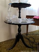Photo of vintage black wood two-tier side table displaying assorted vintage glassware including candlesticks, bowls and dishes.