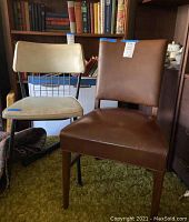 Two vintage chairs side by side, one with brown leather upholstery and wooden legs, the other with light-colored padded seat and black metal frame