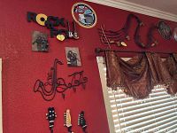 Wide shot of multiple music-themed wall decorations including  'ROCK AND ROLL' sign, Fender sign, saxophone and music note metal art, and part of a curtain.