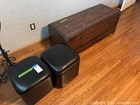 Photo showing brown tufted storage bench and two black square storage ottomans on wooden floor against wall.
