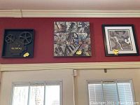 Wide view of three wall art pieces on a red wall above door featuring vintage movie reels shadow box, musical collage painting, and monochrome musical instrument print.