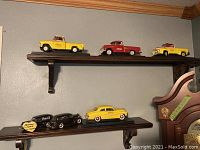 Three diecast trucks on top shelf and partially visible cars on bottom shelf