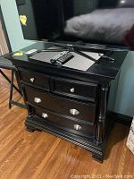 Front view of the black dresser showing two smaller top drawers and two larger bottom drawers, with metal handles and decorative columns on sides.