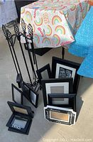 Photo showing six black picture frames of various sizes and four black metal fireplace tools in a stand with decorative handles.