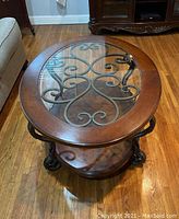 Top view of the oval coffee table showing wood frame, glass top, and black metal scrollwork underneath.