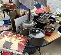 Overview of assortment with pots, pans, muffin trays, and kitchen signs arranged on outdoor table under umbrella