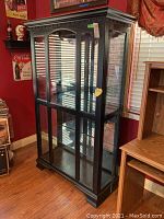 Black wooden curio cabinet with glass panels viewed from front left corner showing overall shape and style.