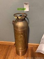 Front view of the brass-colored decorative fire extinguisher showing cylindrical shape and circular guard on top.