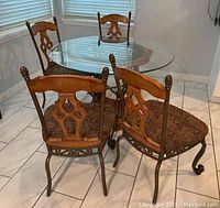Four dining chairs arranged around a round glass dining table, showing metal frames with wooden upper backrest parts and patterned fabric seats.