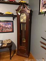 Full view of wooden grandfather clock showing upper case, clock face, and lower glass panel with pendulum and weights