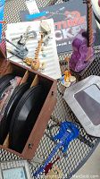Photo showing wooden box with black vinyl records inside, guitar pens, musical note picture frames, and a purple guitar decoration lamp base on a metal table surface.
