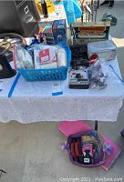 Table with various health and beauty items including a blue basket filled with bandages and cotton products, various boxes, and miscellaneous items. Yoga mat and weights in plastic bag below table.
