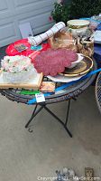 Photo of various holiday partyware items on a lawn chair table, including trays, bowls, plastic flutes, decorative mats, and a rolled Christmas table runner