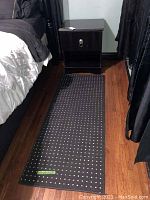 Photo of black runner with white dots placed on wooden floor next to a bed